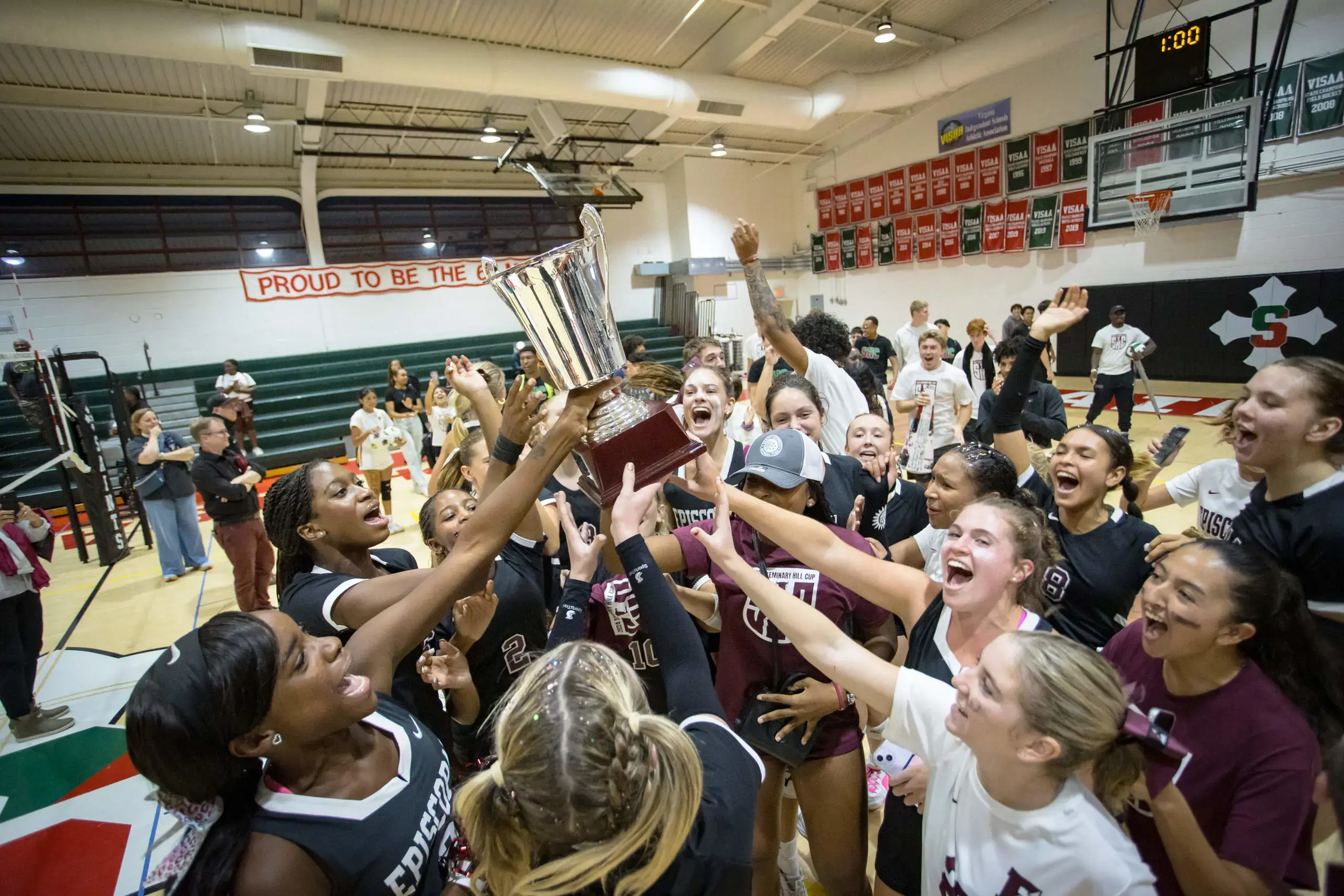 This image is full of energy and celebration! It captures the excitement of a victorious moment, with a group of athletes lifting a championship trophy in a gymnasium. 