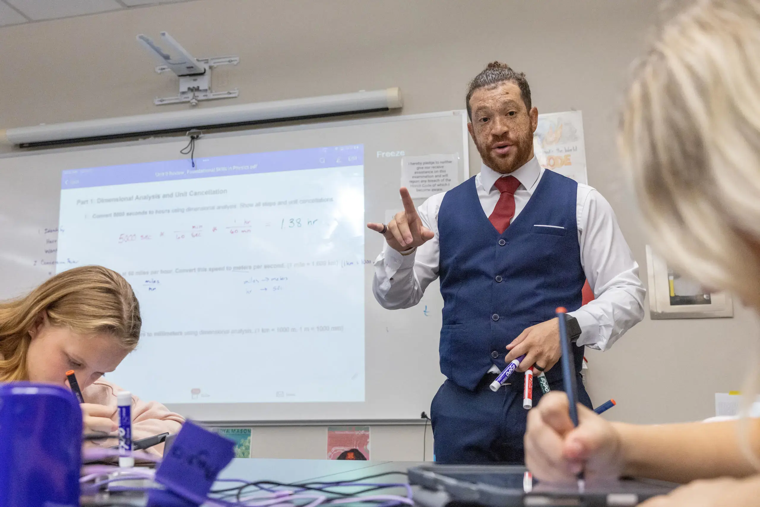 A passionate teacher in a sharp vest and tie brings physics to life, engaging students in an interactive lesson on unit conversions. 