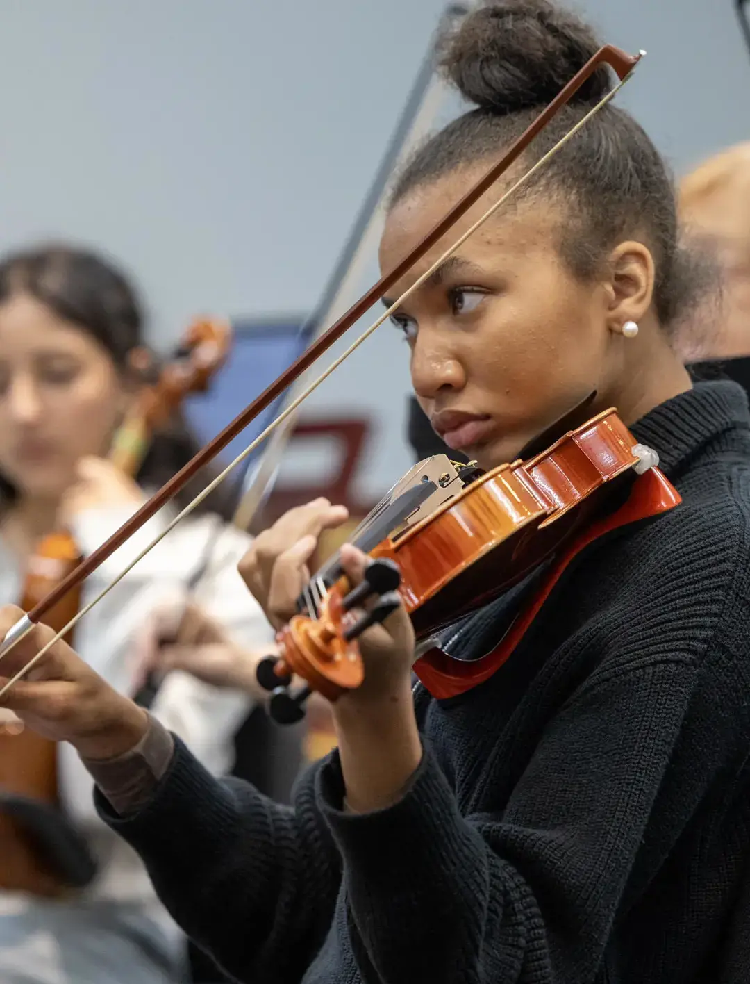 A student violinist, dressed in a black sweater, plays with focus and precision during an orchestra practice.
