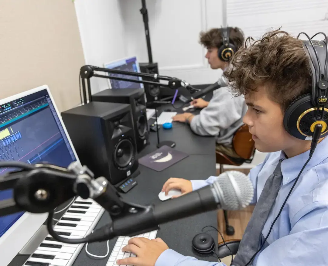 Students engage in music production in a modern recording studio, wearing professional headphones and working on digital audio workstations.