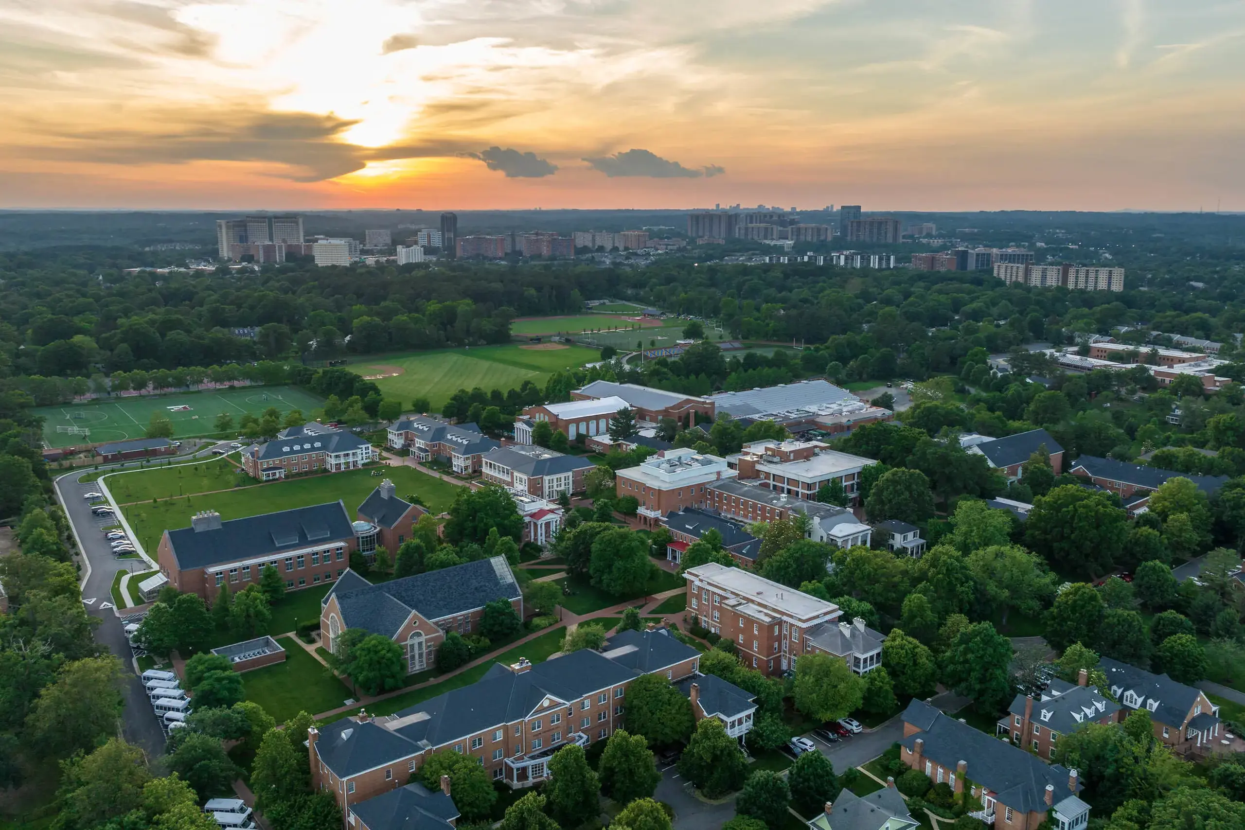 An aerial view of Episcopal High School’s picturesque campus at sunset, featuring red brick buildings with dark roofs surrounded by lush green trees. 