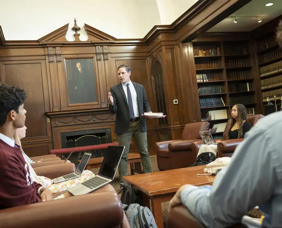 A teacher leads an engaging discussion with students in a wood-paneled library setting, fostering critical thinking and intellectual curiosity at Episcopal High School.