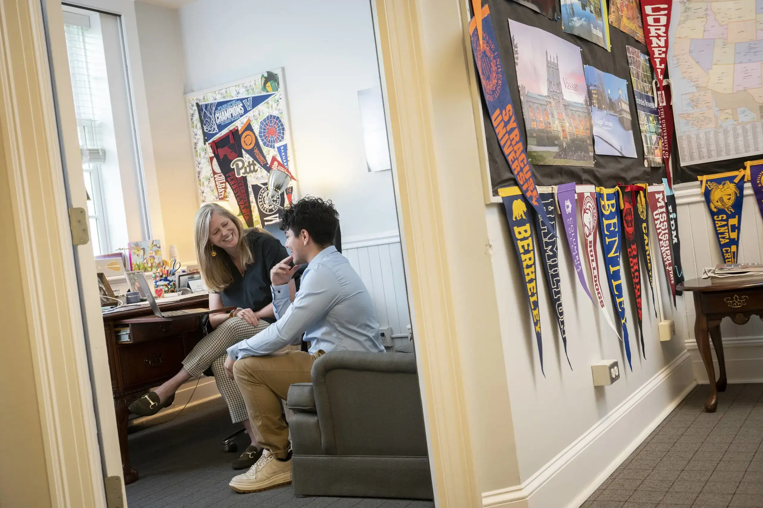 A student meets with a college counselor in a warmly decorated office, discussing future academic plans. 